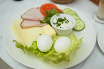 Healthy breakfast with boiled eggs with green salad, cucumber and shank. Latte coffee and fresh cereal bread in the background.