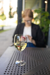 Elegant blonde lady with glass of white wine in restaurant. Aesthetic glass of white wine or water with blurry city cafe background. High quality photo