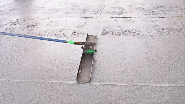 Worker is holding a steel fresno concrete trowel and smoothing plastering over freshly poured concrete that is wet in construction zone