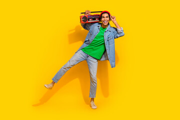Full body photo of attractive young man hold tape recorder dancing wear trendy jeans clothes isolated on yellow color background