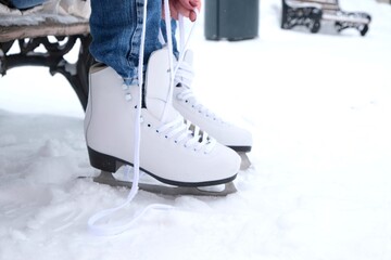 A woman sitting on a bench in the park puts on figure skates and ties her shoelaces with her hands, close-up view - obrazy, fototapety, plakaty