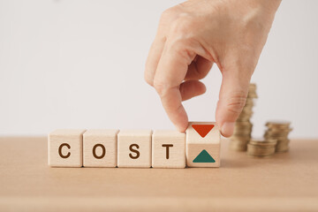cost word on wooden cube blocks with hand flipped to change arrow sign and blurred stack of coins...