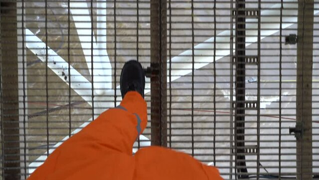 Legs in orange coverall walk on metal grate. RIG. Industrial area