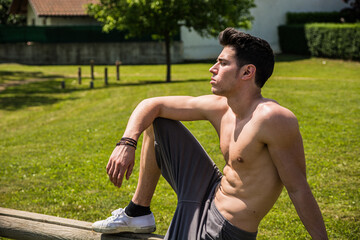 Obraz premium A shirtless man sitting on a bench in a park. Photo of a man enjoying a peaceful moment on a park bench