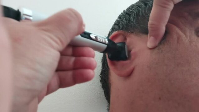 Removing hair from the ears with trimmer. Barber uses machine to cut hair from the ear.