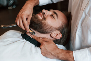 Fototapeta na wymiar On the neck, shaving the beard. Man is visiting modern barber shop. Modern style