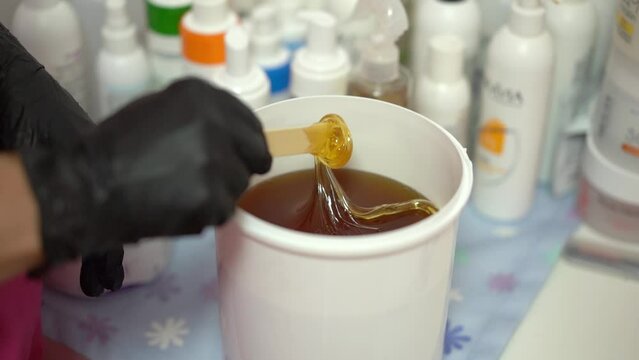 The hair removal specialist stirs sugar paste with wooden stick. Sugaring salon