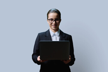 Teenage female student in formal style using computer laptop, on grey background