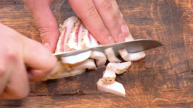Slicing of salted pork fatback on cutting board, close-up. Ukrainian traditional food - salo