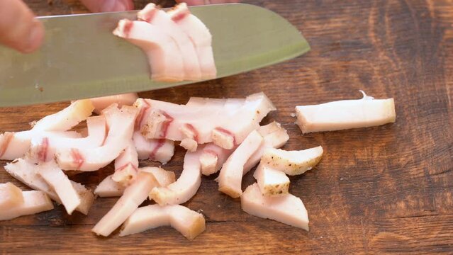Slicing of salted pork fatback on cutting board, close-up. Ukrainian traditional food - salo