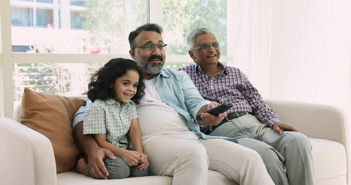 Multi-generational men spend time together switch channels, enjoy movie using on-line digital streaming TV on weekend at home. Cute little boy with grandpa and great-grandad watch cartoons on leisure