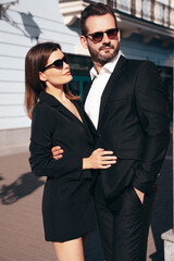  Beautiful fashion woman and her handsome elegant boyfriend in black suit. Sexy brunette model in jacket. Fashionable smiling couple posing in street. Brutal man and female outdoors. In sunglasses