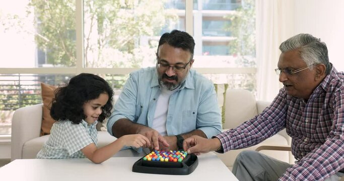 Loving multi-generational Indian family sit at table play rainbow balls boardgame with preschooler boy, enjoy IQ board game to improve children cognition, boost concentration. Intellectual activity