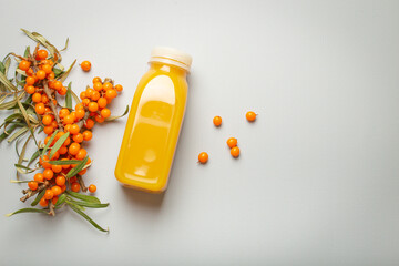Sea buckthorn healthy juicy drink in bottle and branches with leaves and ripe berries top view on light grey simple background. Space for text.. - obrazy, fototapety, plakaty