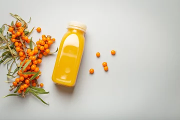 Foto op Plexiglas Sea buckthorn healthy juicy drink in bottle and branches with leaves and ripe berries top view on light grey simple background. Space for text.. © somegirl
