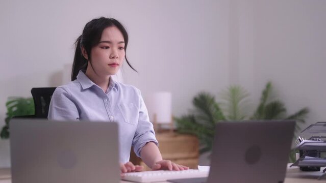 relaxed young Asian woman sitting in her living room while working with a laptop computer at her desk stretching her arms for prevent Office syndrome after working long time at home.