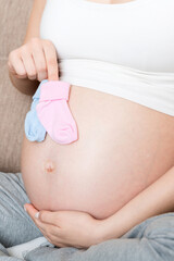 beautiful pregnant young woman holding a pair of cute baby socks on her tummy, lying on sofa at home