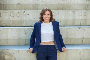 Portrait of a successful business woman in front of modern business building. Young manager poses outside. Woman employee of an office.