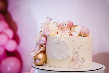 Birthday cake for 1, 2, 3 old year. Cake is decorated with rabbit figure, butterfly, flowers, golden decor for girl. Delicious reception at birthday party. Trendy cake on background of pink balloons.