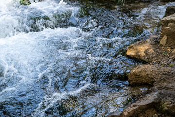 A stormy stream of a mountain river flows over large and small stones, white waves, strong current, small waterfalls, swirls, dark water