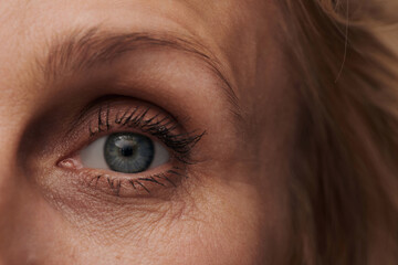Close-up of blue eye of mature woman with expression lines, first wrinkles, anti-aging cosmetics concept - obrazy, fototapety, plakaty
