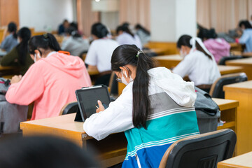 Rear view of university students concentrate on doing examinations via tablet and smartphone in the classroom - obrazy, fototapety, plakaty