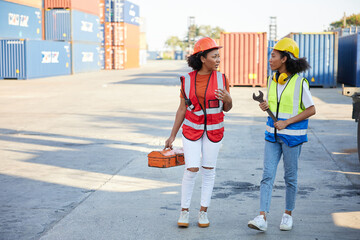 young female African factory workers or engineer holding tools and talking about work in containers warehouse storage