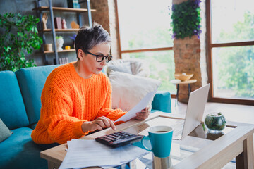 Photo of serious confident mature lady dressed orange sweater counting bills calculator indoors...