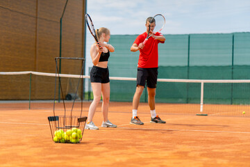 a young coach teaches a beginner girl to play tennis, practice movements with a racket practice...