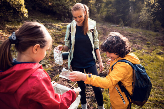 Young Caucasian mother and her children cleaning and recycling plastic while hiking in the woods