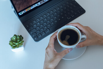 Drink coffee at her desk while working on a tablet. Working online on white table at office. Blogger. Journalist. Online job.