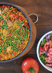 Close up view from above of paella and tomato salad. Rice with pork and chicken, vegetables and peas. Spanish food.