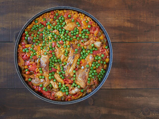 Rice with pork and chicken, vegetables and peas. Mediterranean food. Spanish paella on round pan seen from above on wooden table.