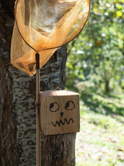 Funny face with glancing eyes and grimace on the mouth drawn on a wooden bucket next to a butterfly catcher. Concept of trapped.