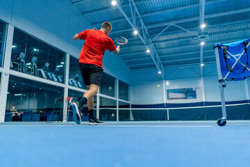 Obraz premium young man on an indoor tennis court hitting the ball with a racket serving during a game tennis instructor professional sport