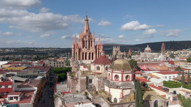 Aerial view of San Miguel de Allende in Guanajuato, Mexico, orbiting around historic landmark Parroquia de San Miguel Arcangel church on a sunny day.
