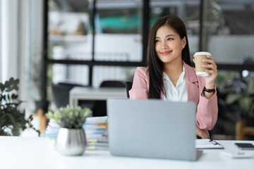 Confident Asian businesswoman working for a real estate project Financial business, accounting and drinking coffee while working, sitting and relaxing, taking a break at the desk.