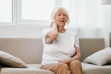 Elderly woman severe neck pain sitting on the sofa, health problems in old age, poor quality of...