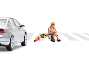 Woman with a grocery bag and injured knee sitting on a street in front of a car