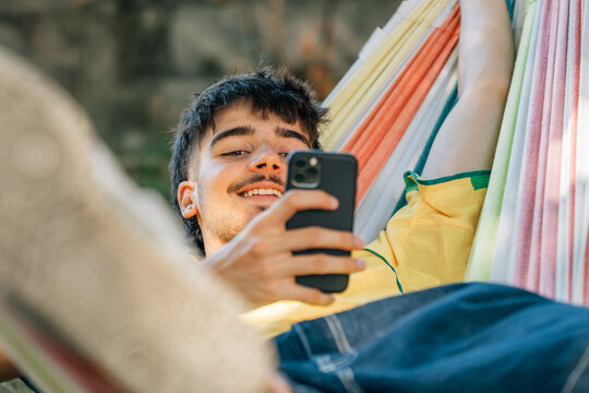 young man in summer in hammock resting relaxed with mobile phone