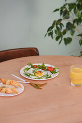 Healthy breakfast of fried egg with tomatoes and green on white plate, orange juice and bread on wooden table in green background.
