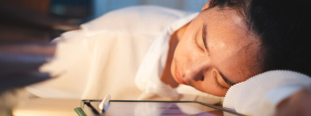 Asian female businesswoman, student or employee is sleeping while working on desk. Concept of exhausted from deadline work, overwork document or overtime late at night. Manager tired of midnight job.