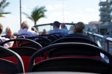 Obraz premium Double decker hop on hot off bus with open roof with some defocused passengers in rear view. On the background there is a palm tree against clear sky. Tourist bus cutout with focus on the foreground.