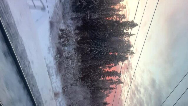 Winter train journey. Houses and winter forest flash by the window. View from the train window on the winter landscape. Winter sunset from the train window. Russia 2023