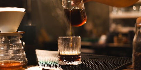 Barista pours hot coffee filter or americano to a glass in loft aroma coffee shop or cafe counter bar. Concept of slow bar, coffee caffeine. Black and brown style. Preparation of coffee ready to serve
