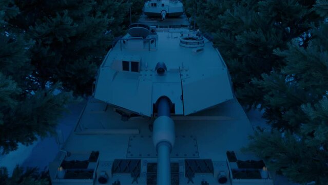 An aerial view over an armored military tank platoon taking cover at night under the spruce trees of a snow-covered road.