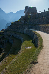 Panorama of the archaeological site of Machupicchu, with view of the terraces, mountains in the background and on top a small house with silhouette of people walking. Peru. Sacred Valley. 
