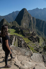 Young woman with long flowing hair, wearing sportswear, with her back turned looking at the archeological site of Machupicchu, Peru. 