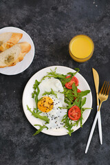 Healthy breakfast of fried egg with tomatoes and green on white plate with orange juice on dark background. Top view.