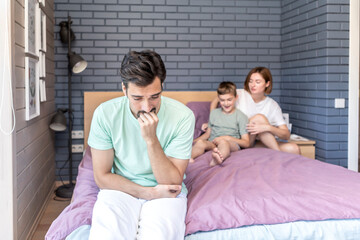 Upset and disappointed man sits on the edge of the bed and he cannot spend time with his wife because their son disturbs them